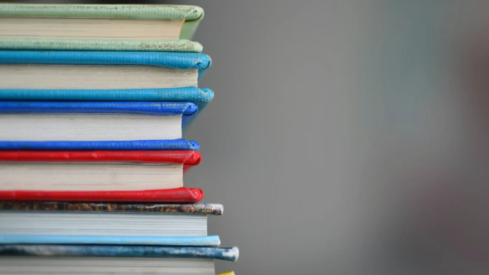 Ein Stapel farbiger Bücher vor einem unscharfen grauen Hintergrund.