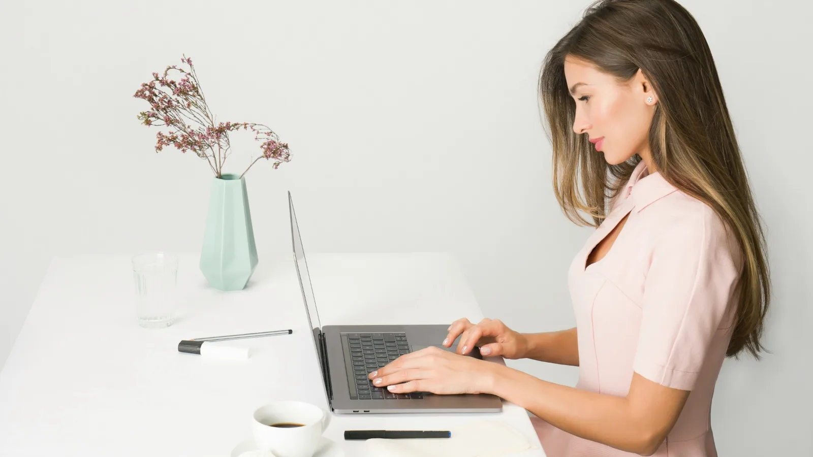 Eine junge Frau arbeitet an einem hellen Schreibtisch am Laptop.