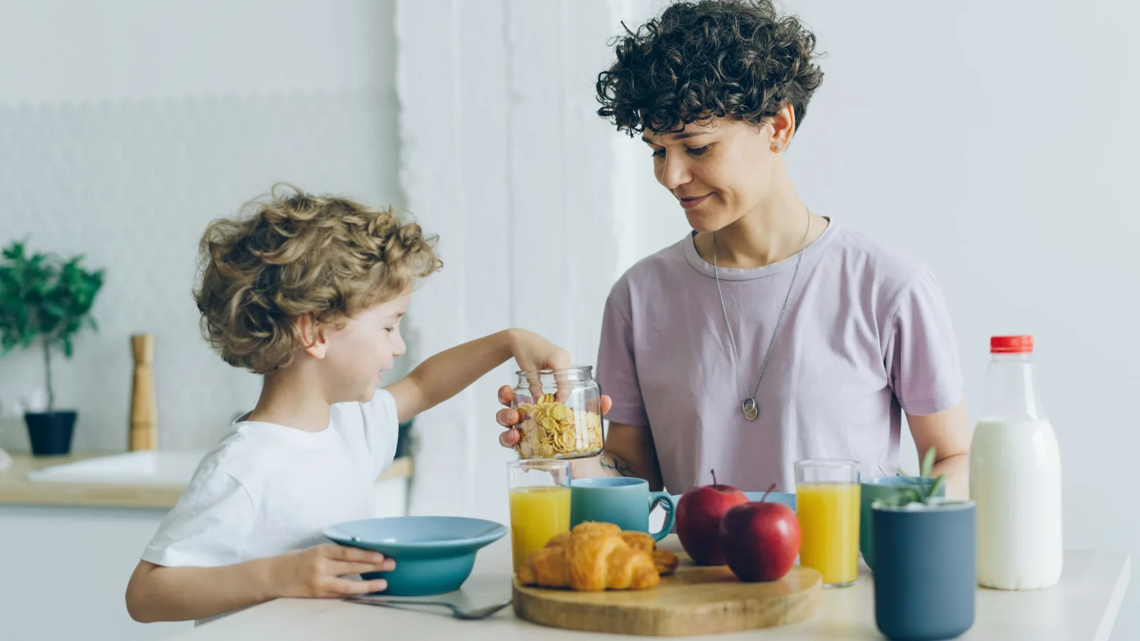 Eine Frau und ein kleiner Junge frühstücken gemeinsam an einem hellen Küchentisch.