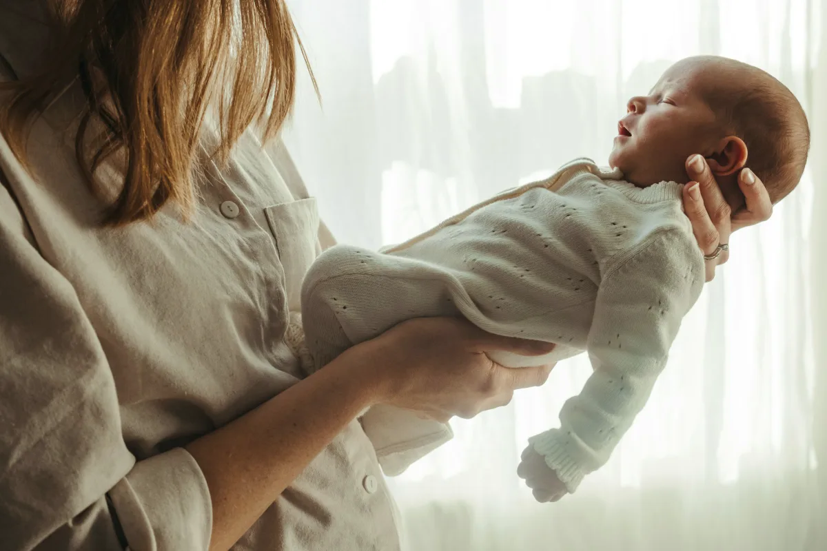 Eine Mutter hält ihr neugeborenes Baby im Licht eines Fensters auf dem Arm.